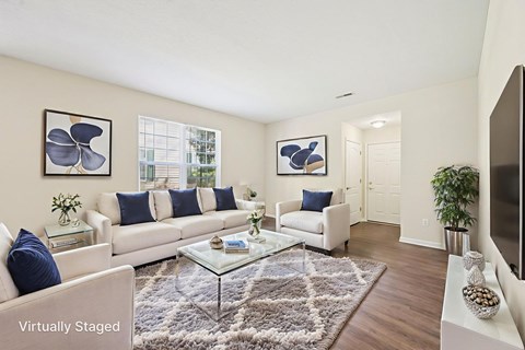 A living room with a white couch, a glass coffee table, and a rug.