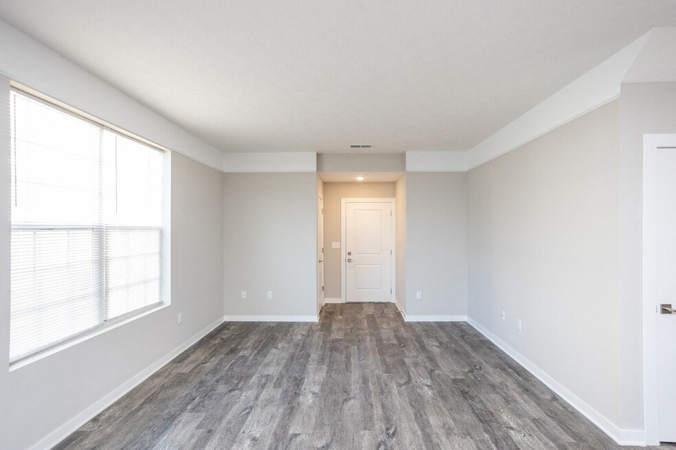 the living room of an empty home with wood flooring and a large window
