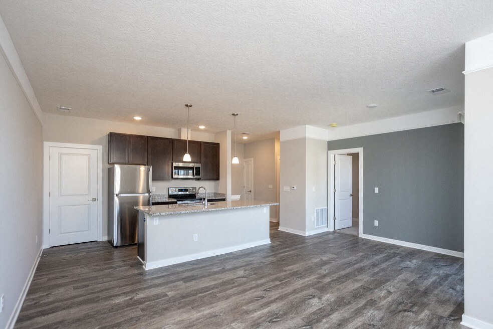 an empty living room with a kitchen and a stainless steel refrigerator