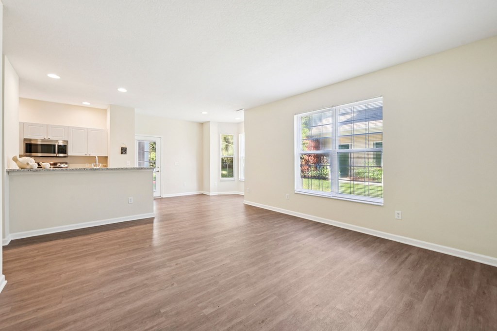A spacious living room with hardwood floors and a kitchen area in the background.