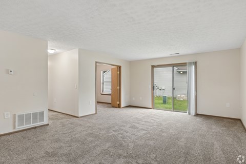 A spacious living room with a carpeted floor and a sliding glass door leading to a patio.