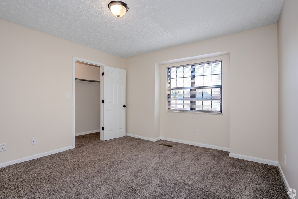 A room with a carpeted floor, a window with blinds, and a door.