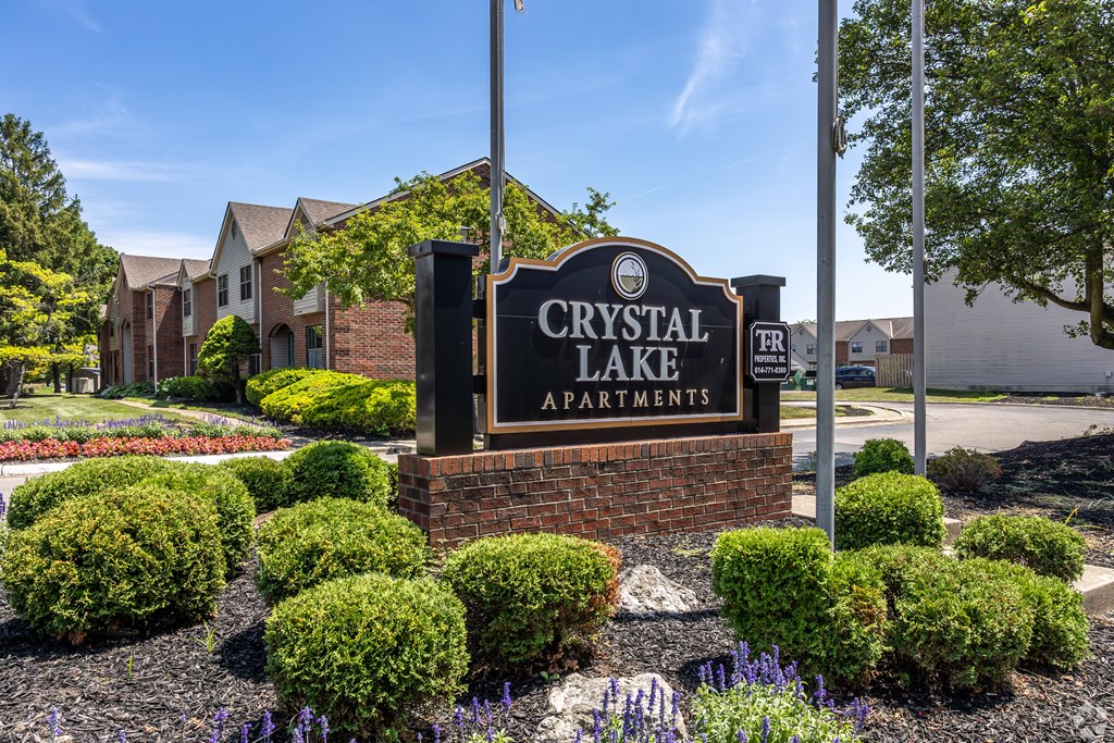A sign for Crystal Lake Apartments is surrounded by bushes and flowers.