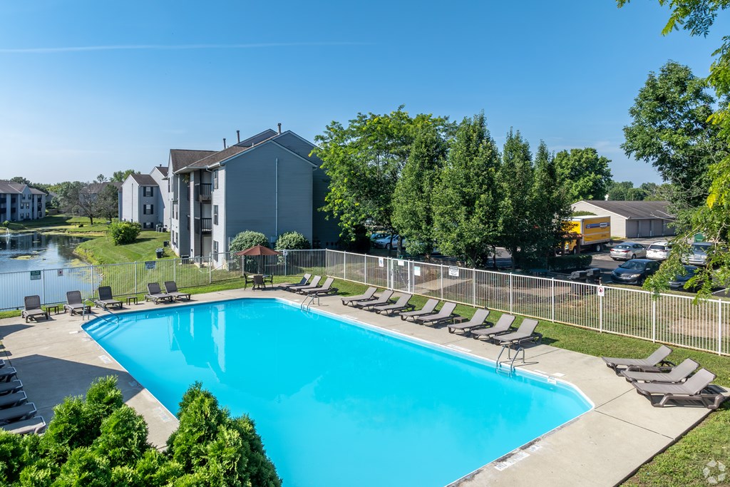 A swimming pool surrounded by lawn chairs and trees.