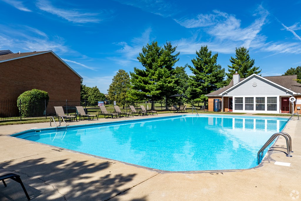A swimming pool in front of a house with trees in the background.