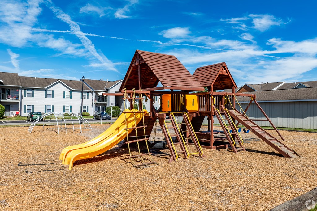 A playground with a yellow slide and a brown roofed structure.