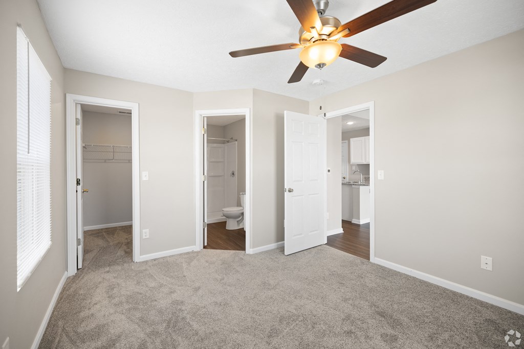an empty living room with a ceiling fan and doors to the bathroom and a closet