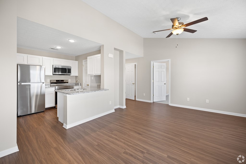an empty living room with a kitchen and a ceiling fan