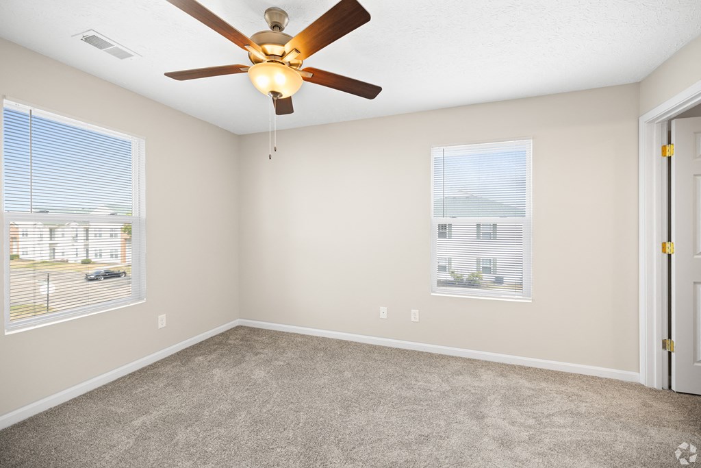an empty living room with a ceiling fan and two windows