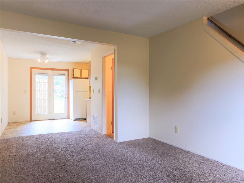 a empty living room with a door to a kitchen