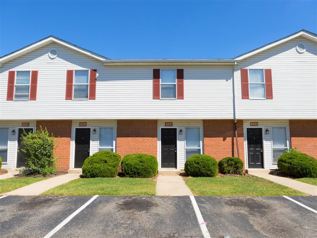 the front of a brick and white building with grass and bushes