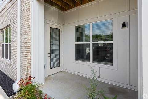 A white door with a window above it and a small bush to the left.