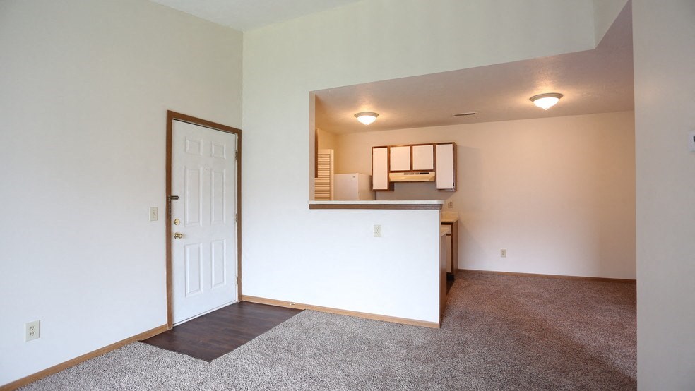 the living room and kitchen of an apartment with carpeted floors