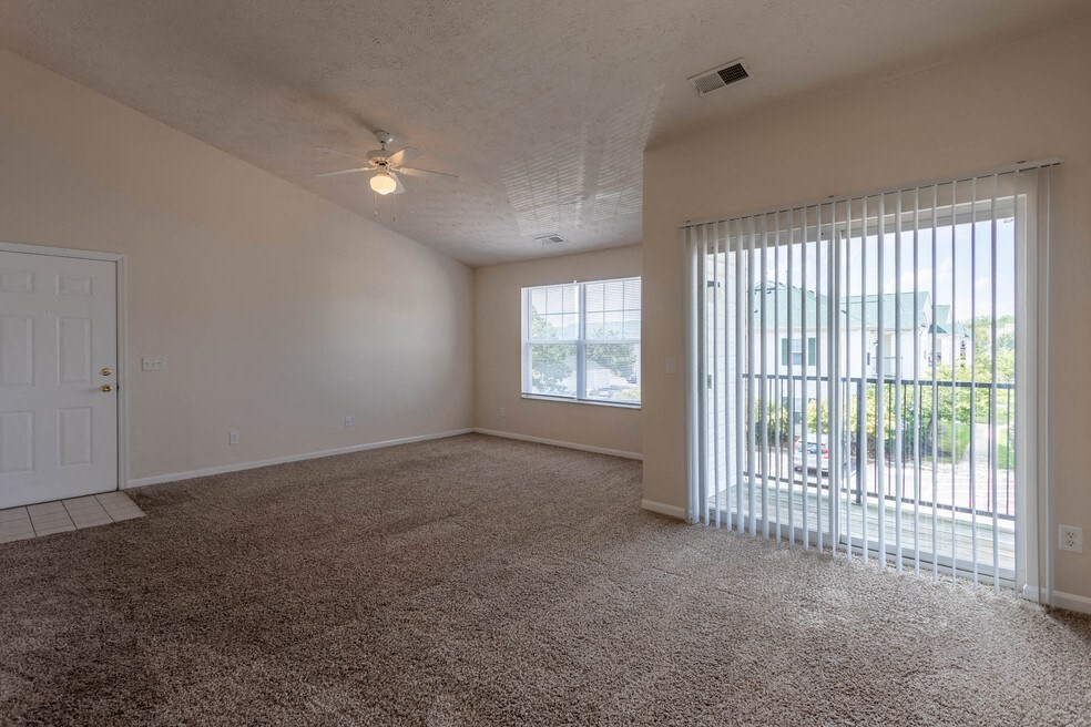 an empty living room with a large window and a ceiling fan