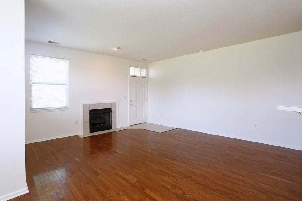 an empty living room with a fireplace and wooden floors