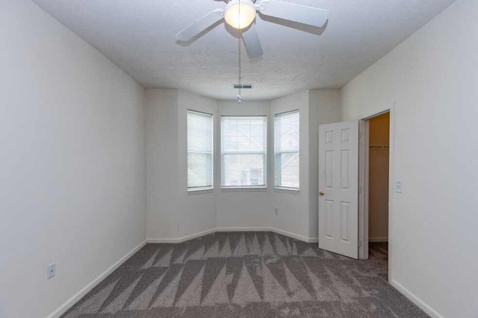 an empty living room with a ceiling fan and windows