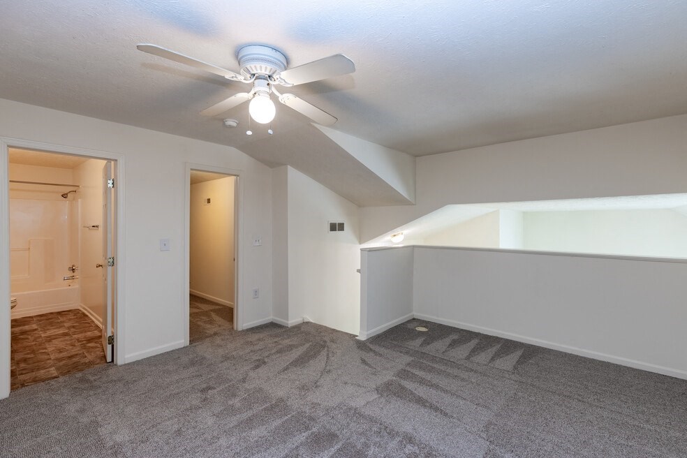 an empty living room with a ceiling fan and a door to a hallway