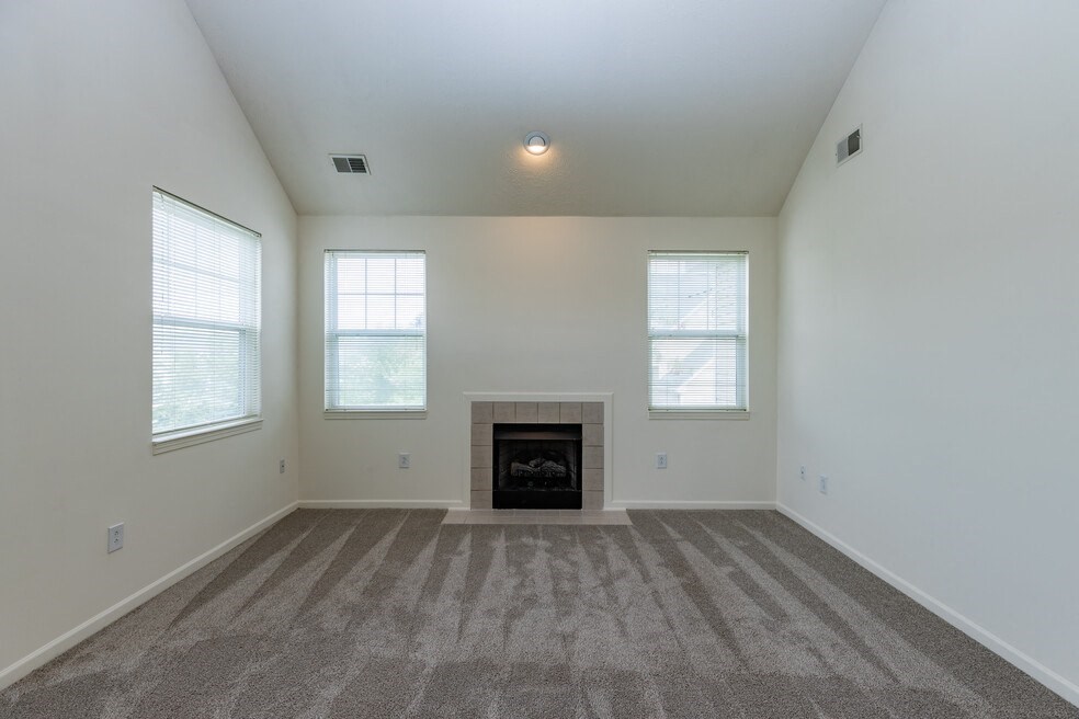 an empty living room with a fireplace and three windows