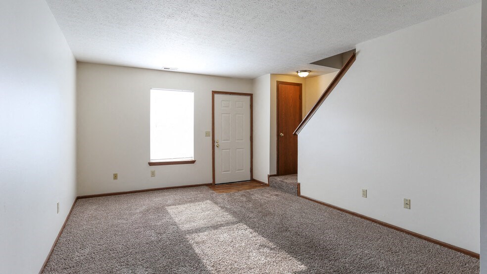 the living room and entryway of an empty house with carpet and a door