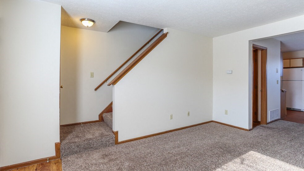 an empty living room with a white wall and a staircase