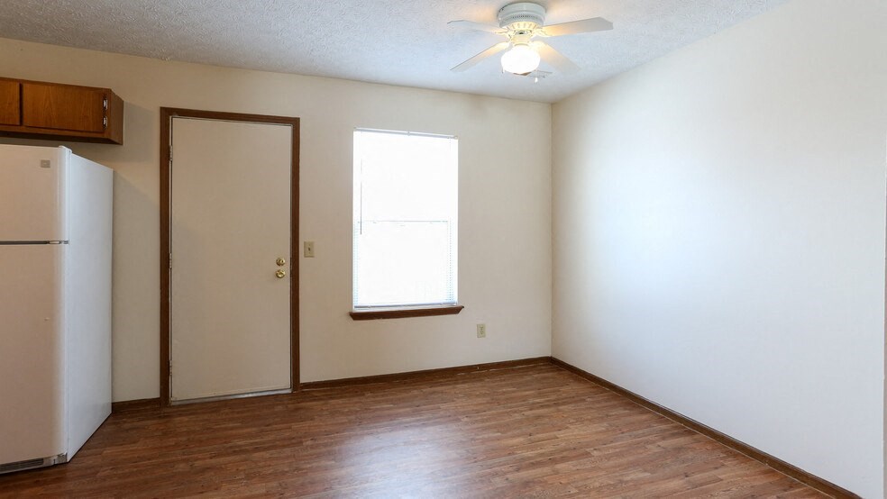 an empty living room with a refrigerator and a ceiling fan