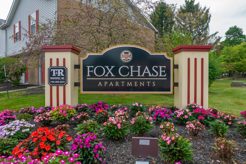 a sign for fox chase apartments in front of a garden of flowers