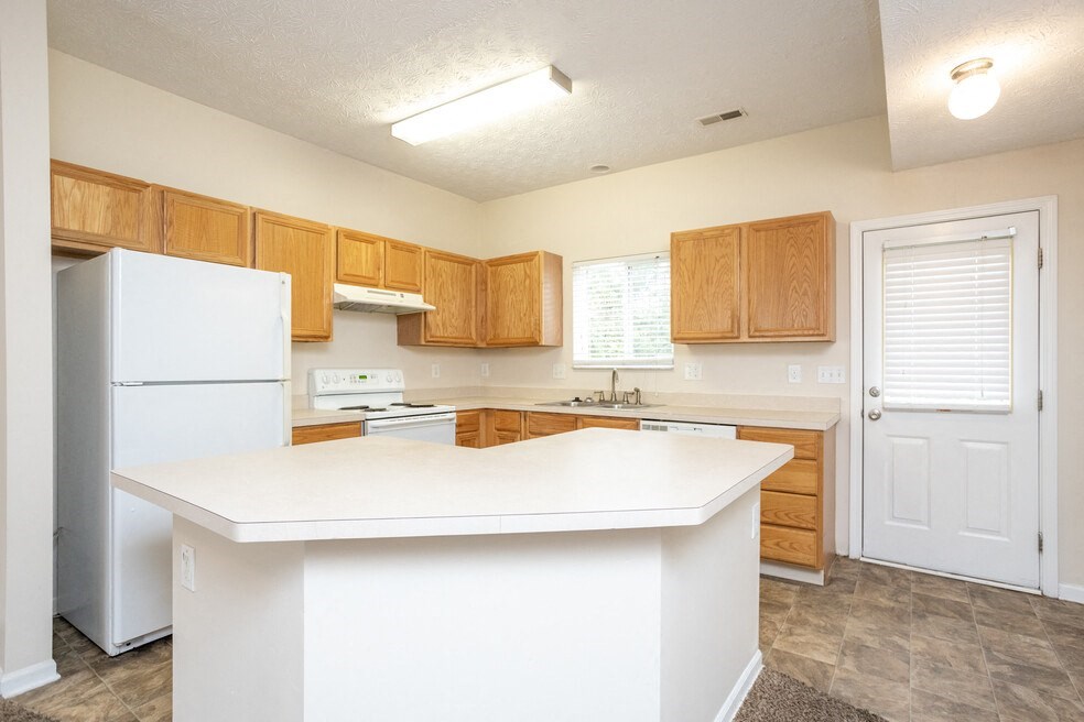 an empty kitchen with a white counter top and a refrigerator