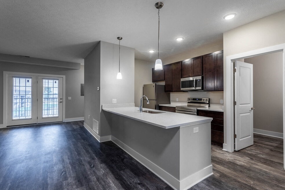 an empty living room with a kitchen and a door to a balcony