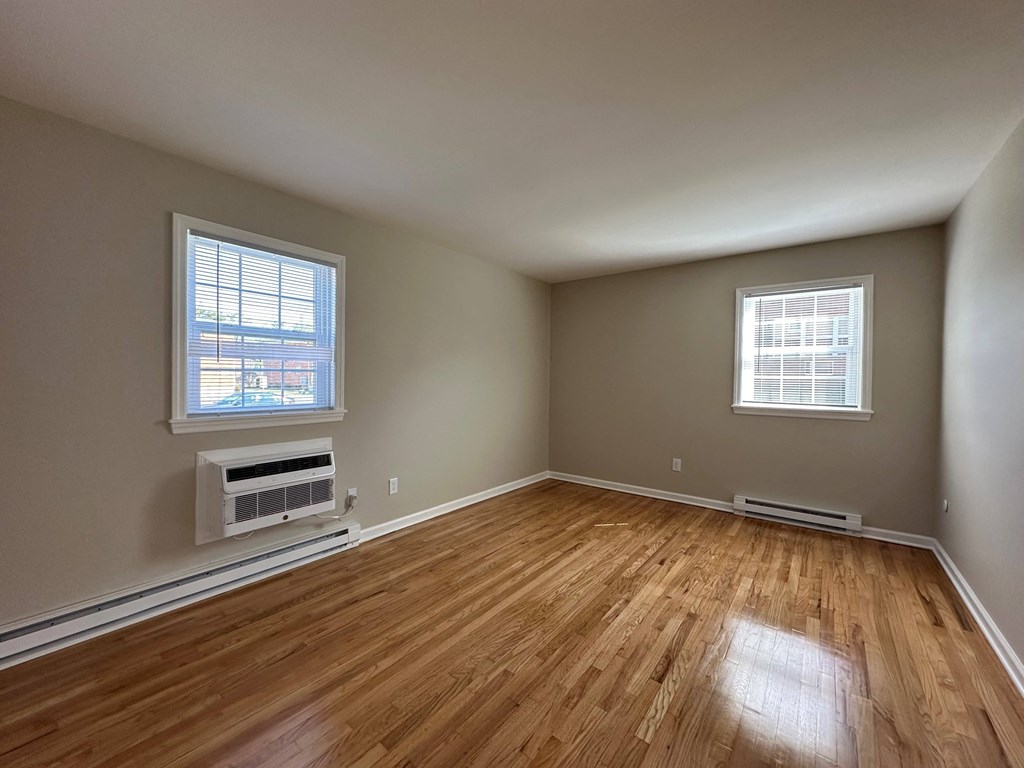 an empty living room with wood floors and a radiator and two windows