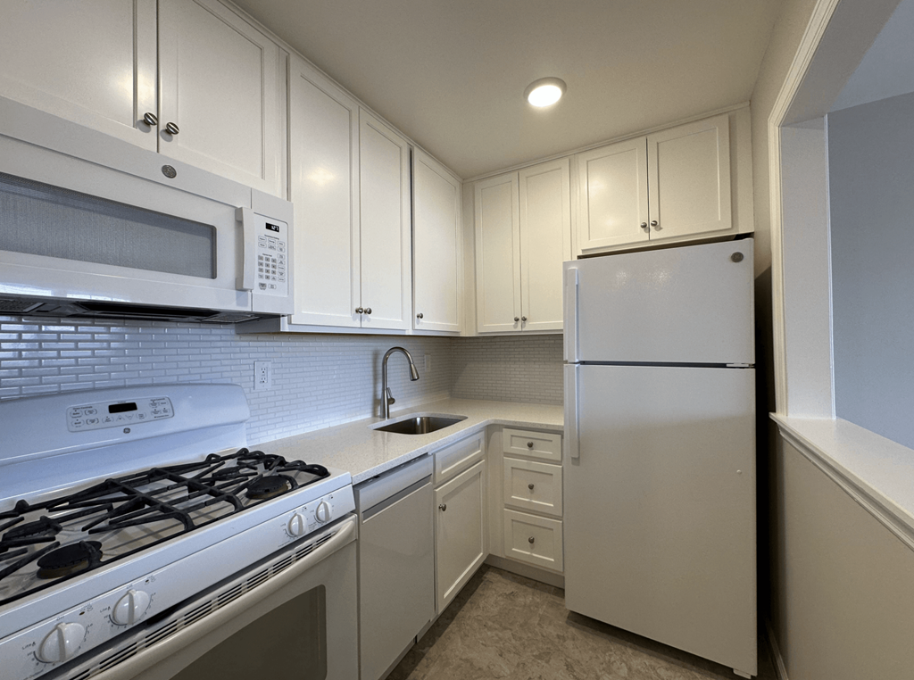 A white kitchen with a stove, microwave, and refrigerator.