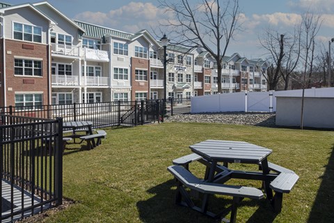 A picnic table sits in the foreground of a grassy area in front of apartment buildings.