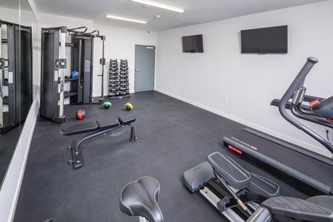 A gym with a variety of equipment including a treadmill, weights, and a bench press.