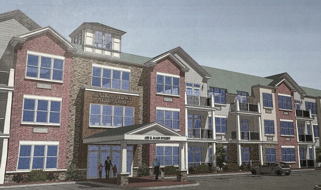 A rendering of a multi-story building with a red brick facade and a green roof.