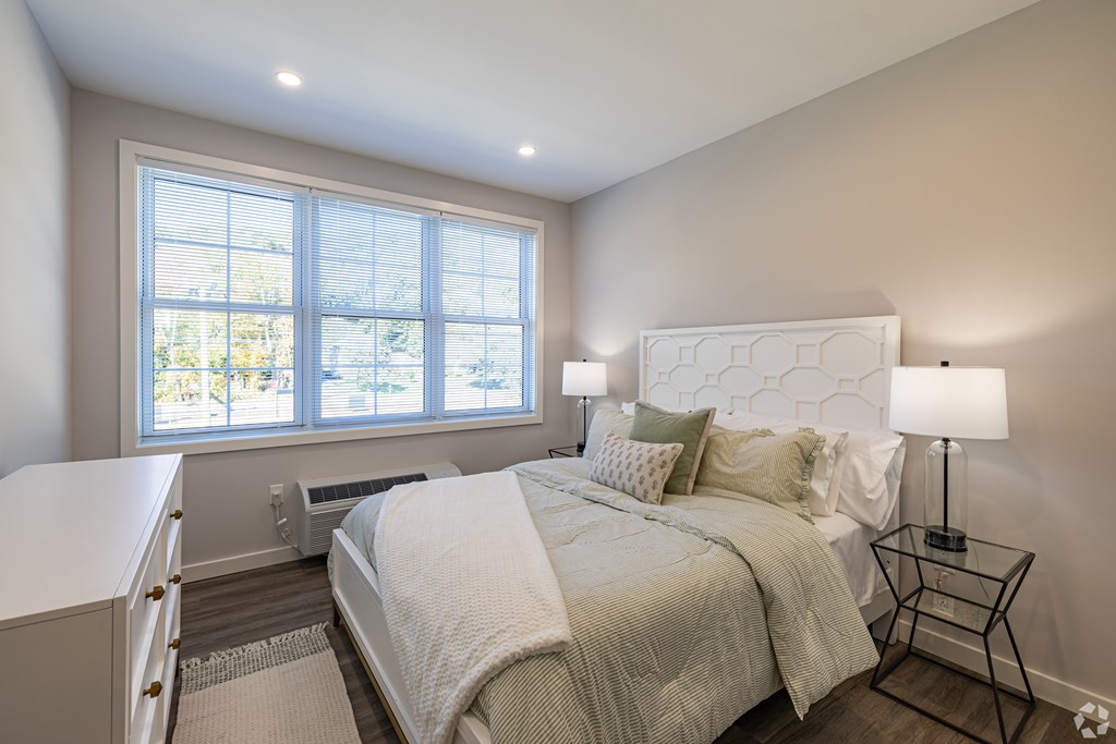 A bedroom with a large bed and a window with blinds.