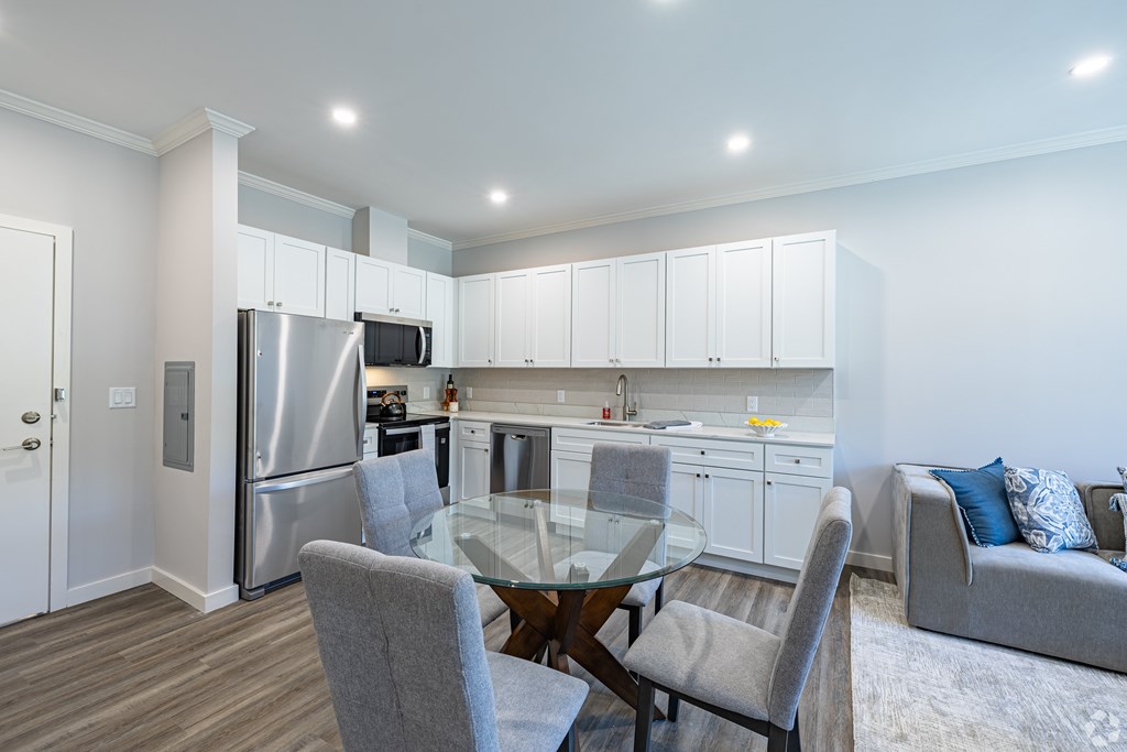 A modern kitchen with a glass table and grey chairs.