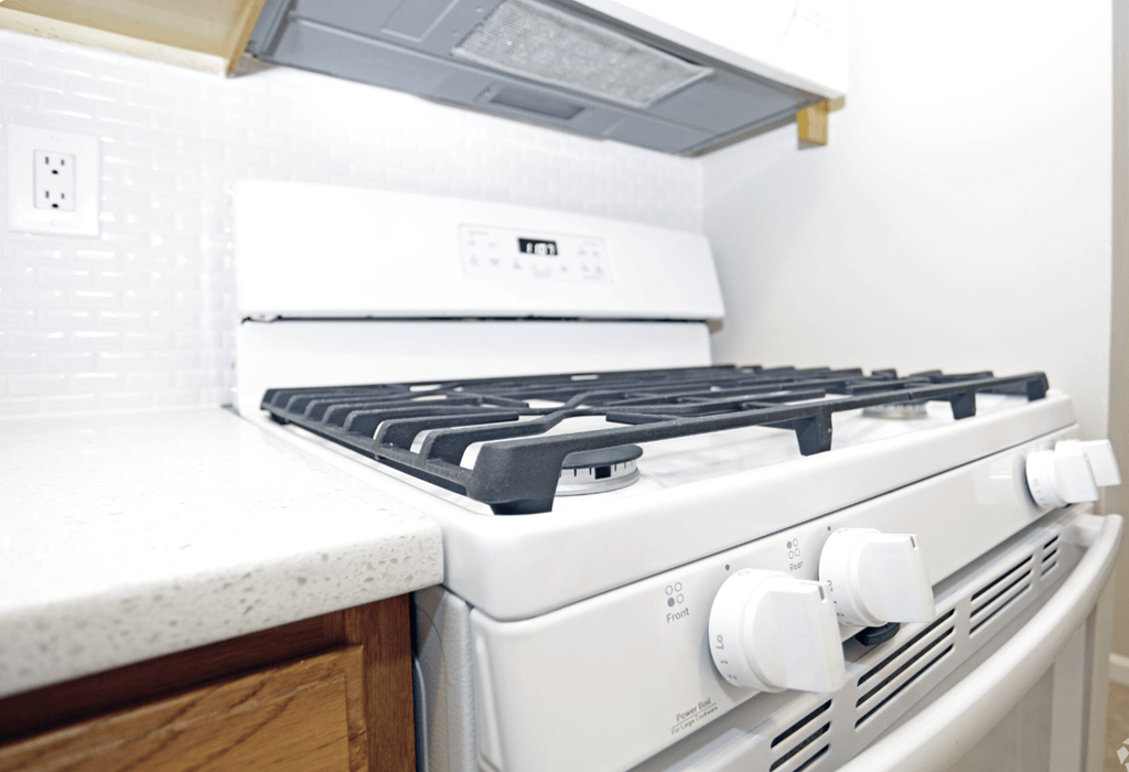 A white gas stove with a white countertop and a white wall in the background.