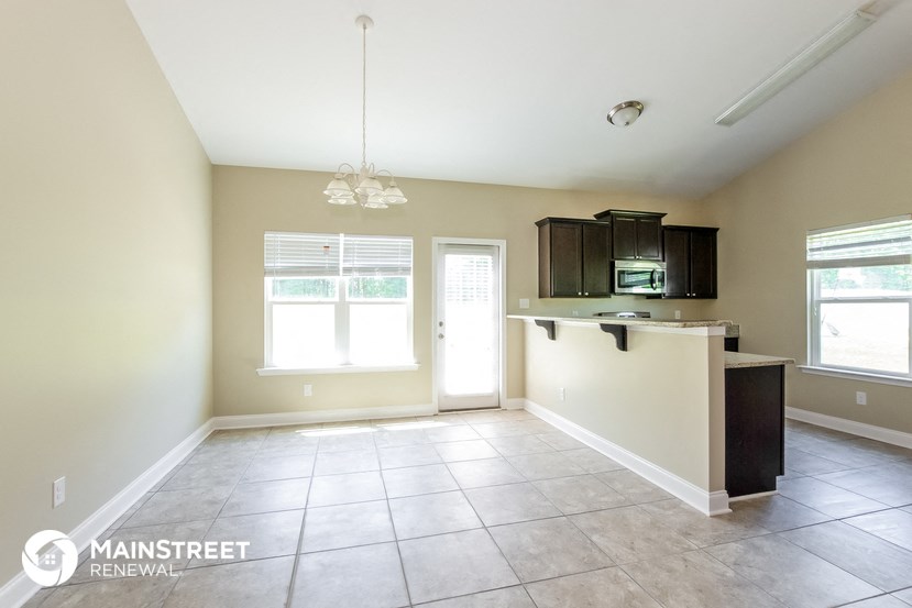 an empty living room with a kitchen and a window