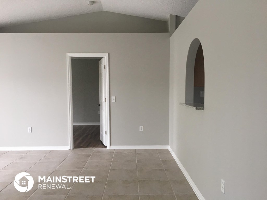 an empty living room with a door to a hallway and an arched doorway