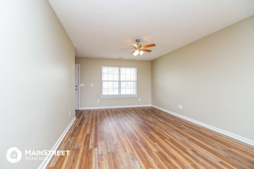 the spacious living room with hardwood flooring and a ceiling fan