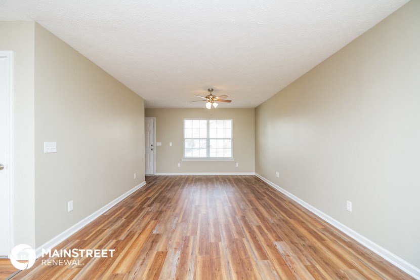 the spacious living room with hardwood flooring and a ceiling fan