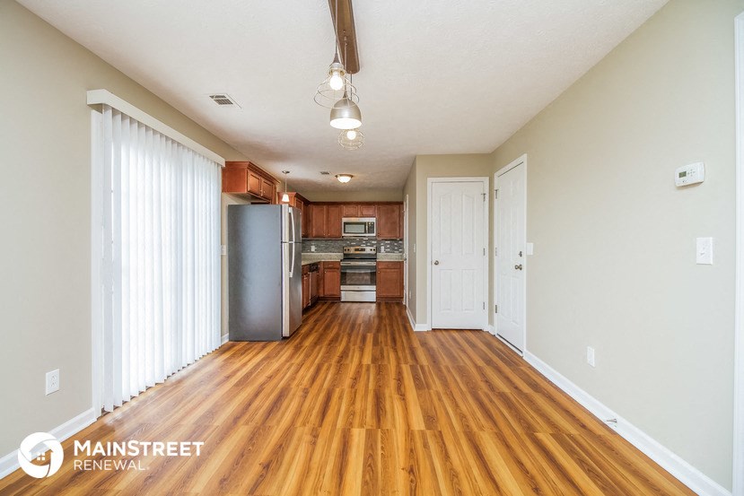 an empty living room with wood flooring and a kitchen