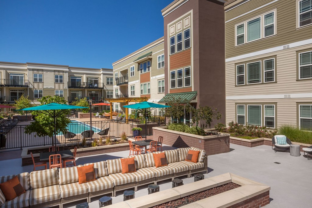 an outdoor area with couches and umbrellas in front of an apartment building