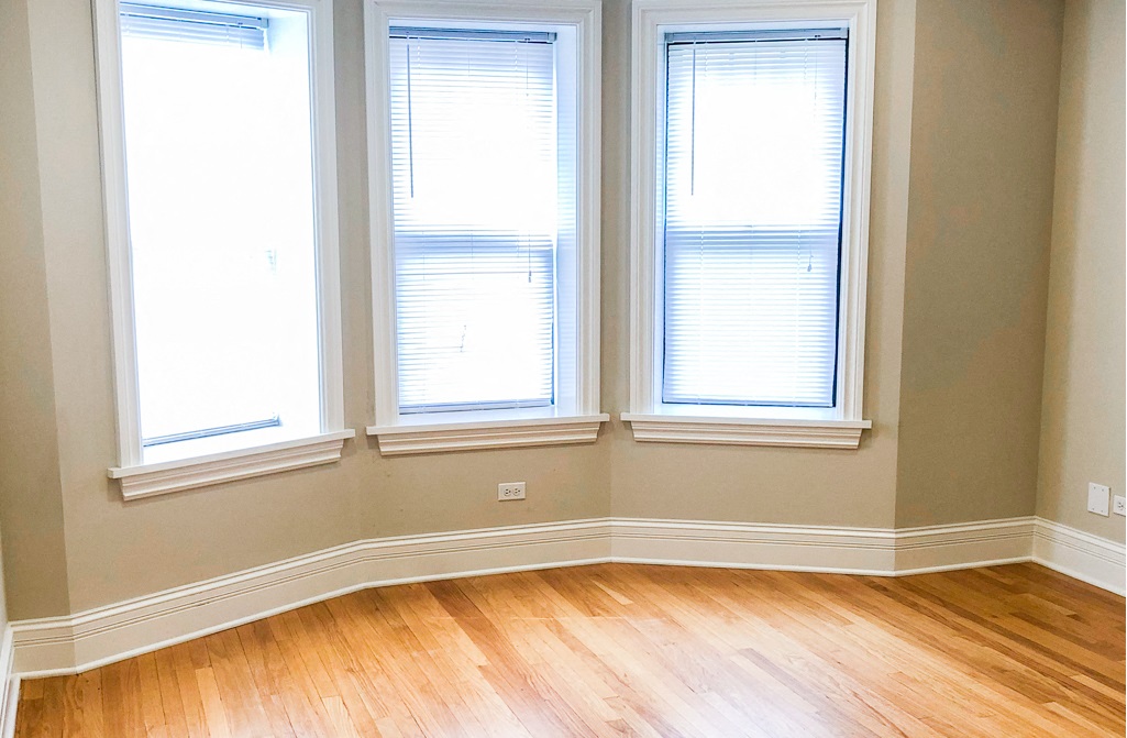 three windows in a corner of a room with a wood floor