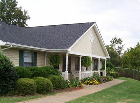 A small house with a porch and a green lawn in front.