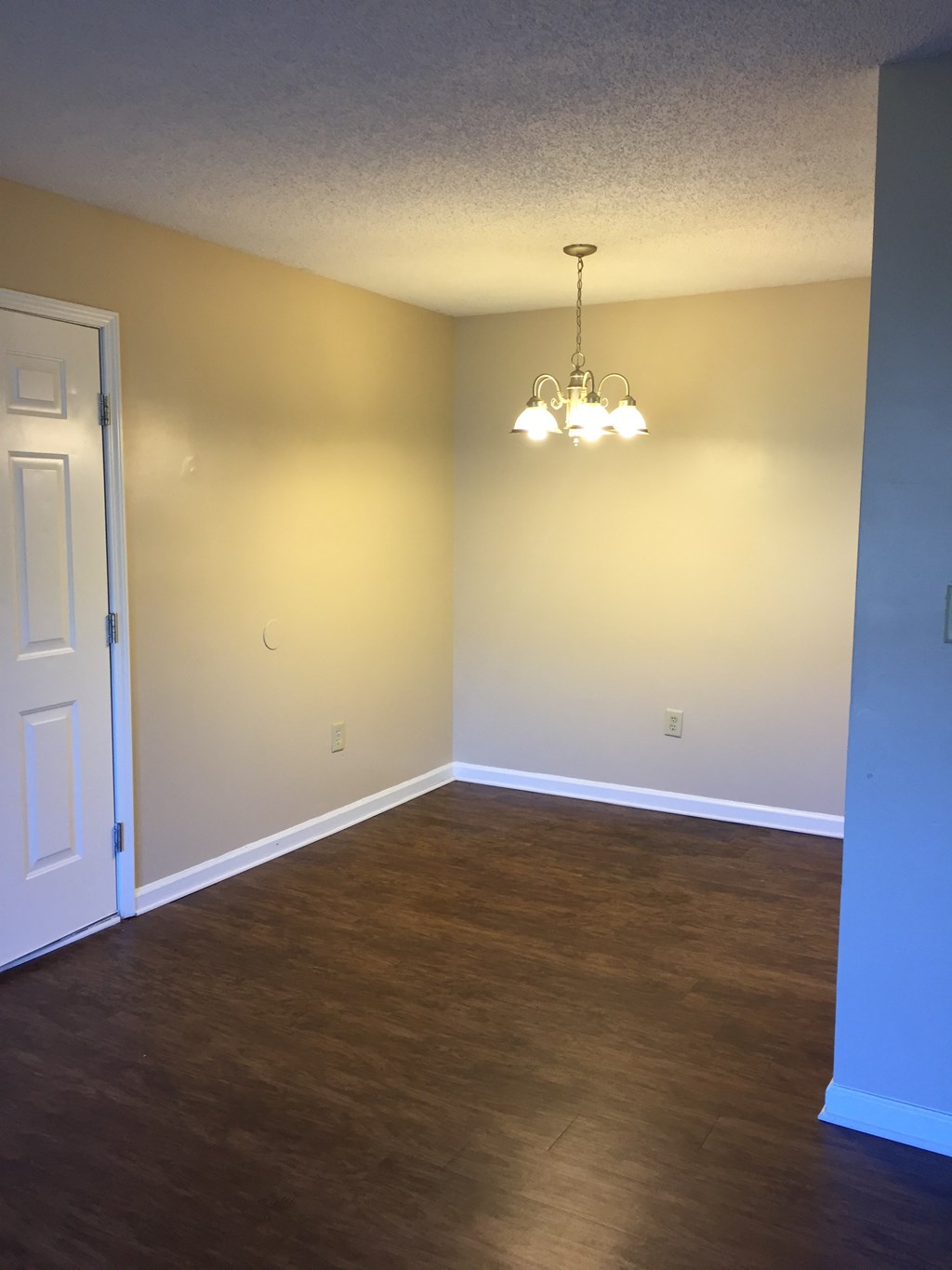 an empty living room with wood floors and a chandelier