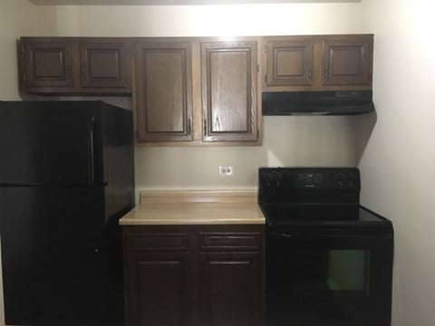 an empty kitchen with wooden cabinets and a black refrigerator
