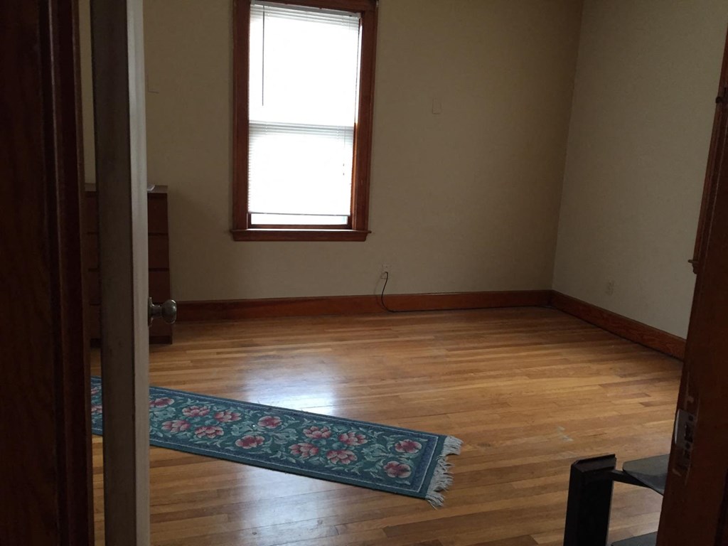 A room with a wooden floor and a rug in front of a window.