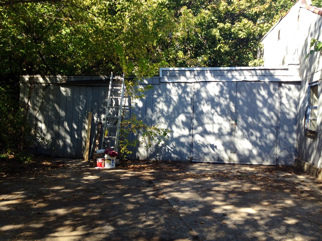 A white bucket with a red lid is on the ground in front of a grey wall.