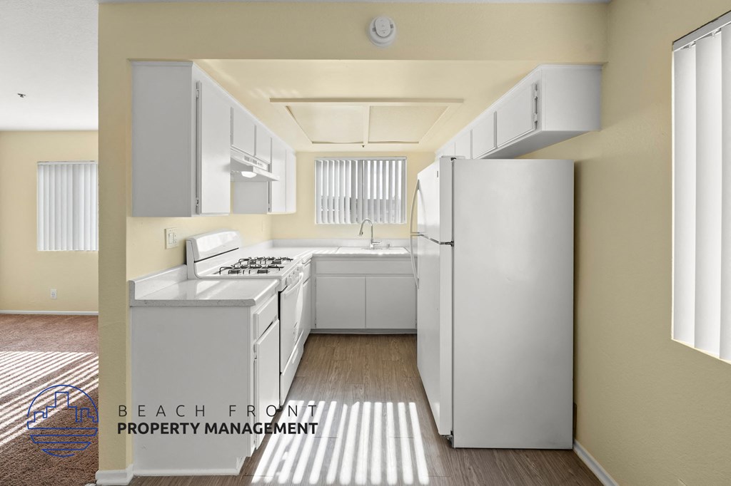A kitchen with white appliances and cabinets with a logo for Beach Front Property Management.
