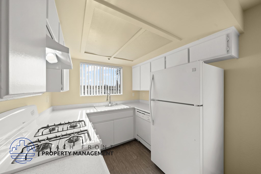 A white refrigerator in a kitchen with a stove top and a window.